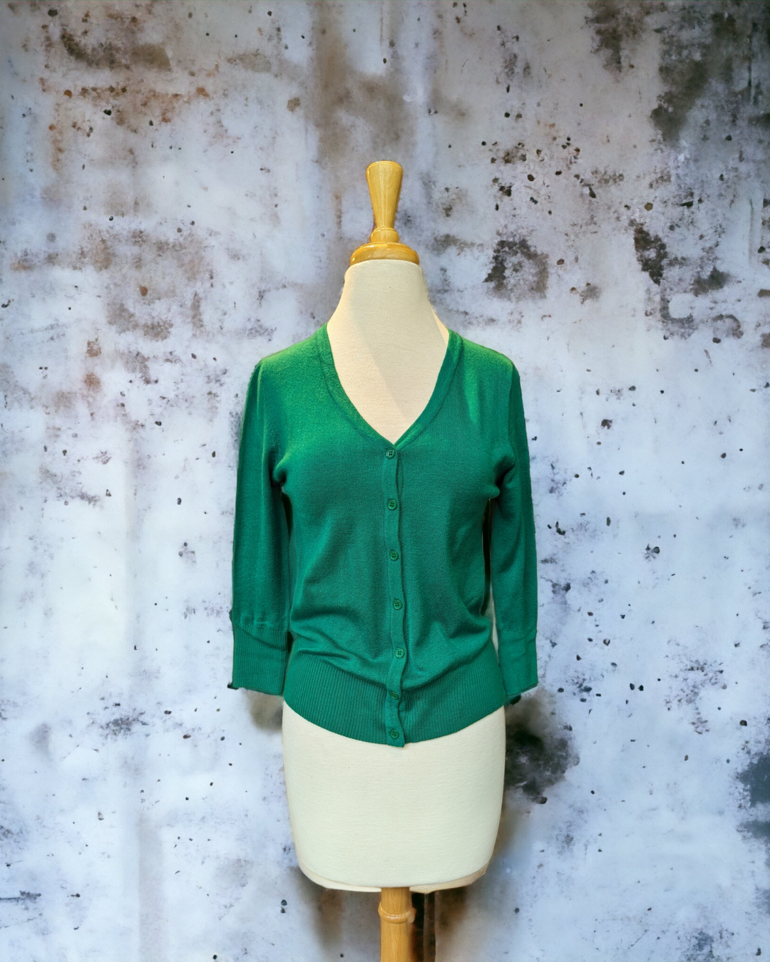 the green cardigan on a bust mannequin in front of a concrete wall