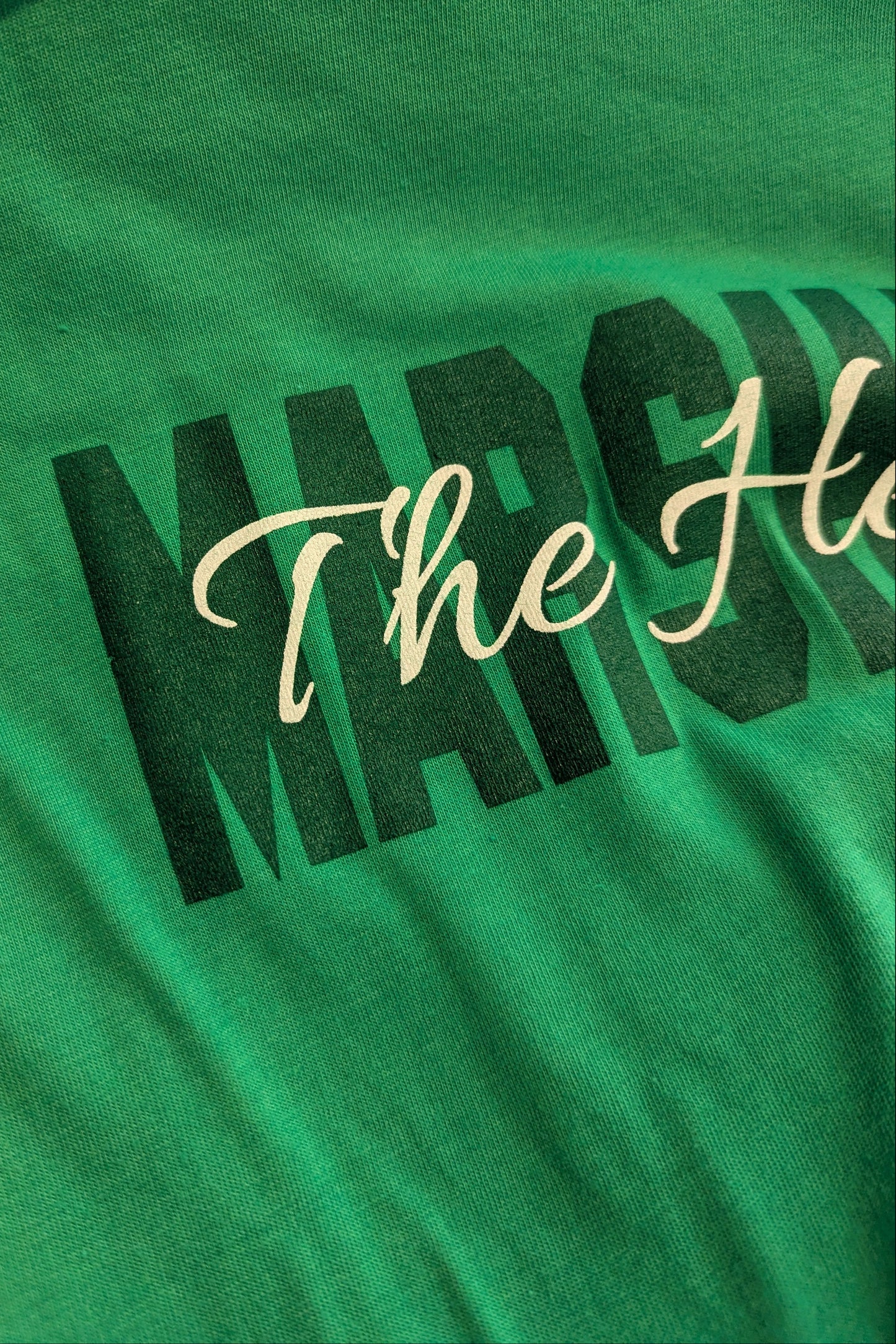 Close-up of a green t-shirt featuring a graphic print with the word 'MARCH' in bold black letters and 'The He.