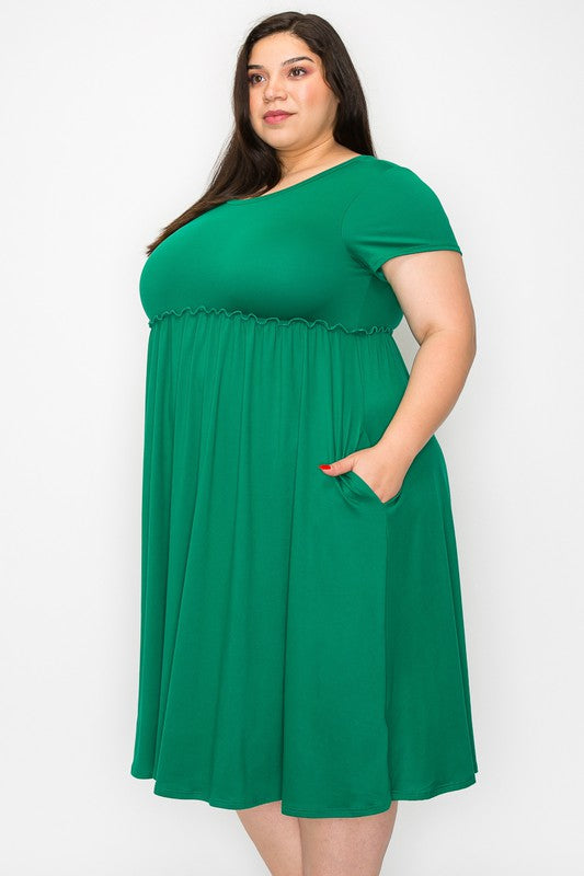 a dark haired model stands in a green dress in a three quarter turn tothe camera