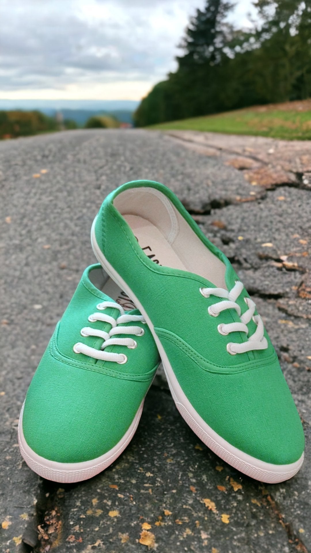 green sneakers sit in a paved road that disappears over the horizon