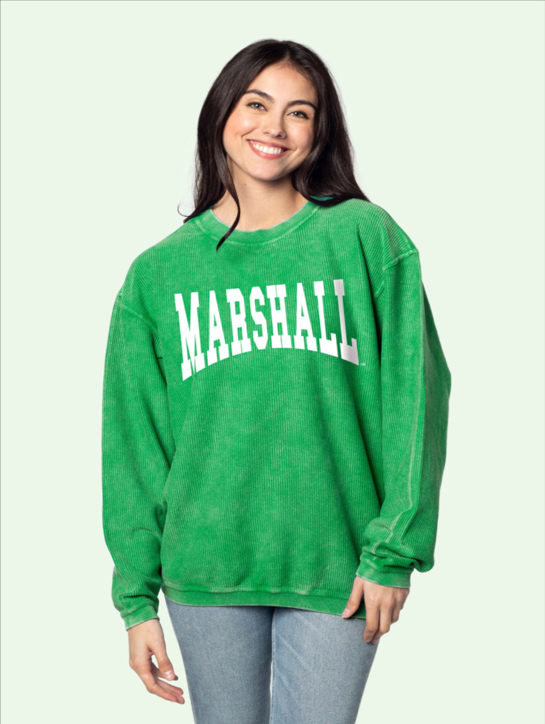A dark haired model stands facing the camera in a kelly green corded fabric pullover jersey with Marshall in curved letters on the front.
