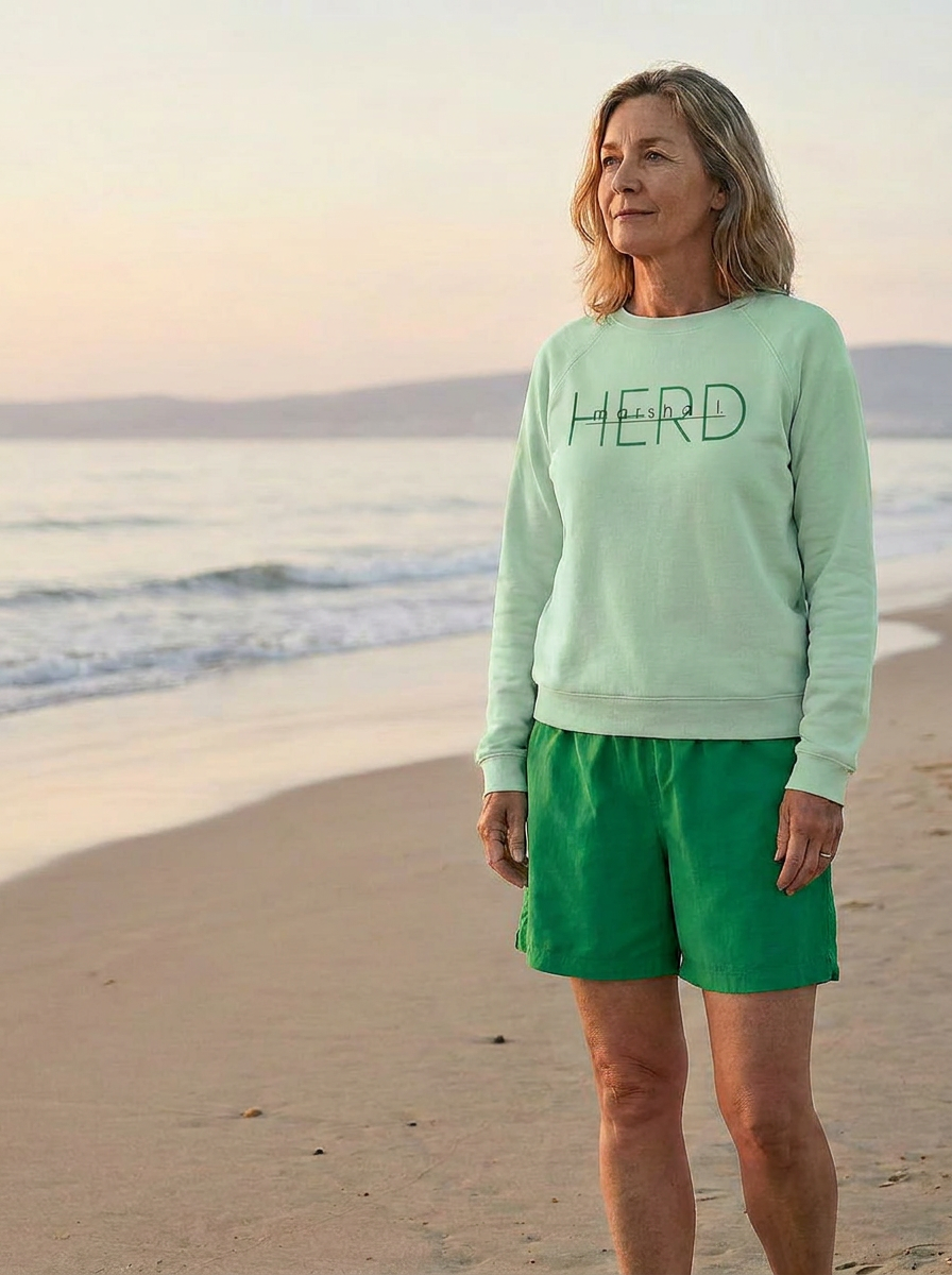 Woman wearing a light green sweatshirt and green shorts standing on a beach.