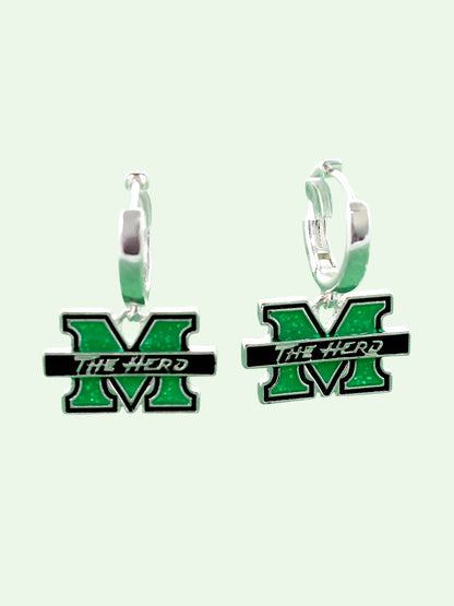 A pair of silver huggie hoop earrings featuring a green and black enamel 'M' charm with the text 'THE HERD' across a black bar, set against a pale mint green background.