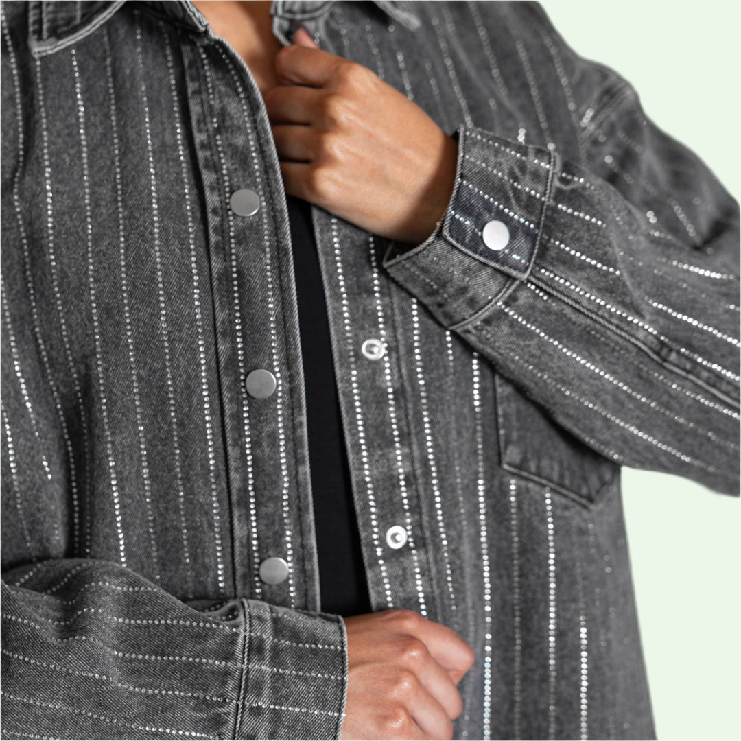 Close-up of a person wearing a gray   denim jacket with rows of rhinestones 