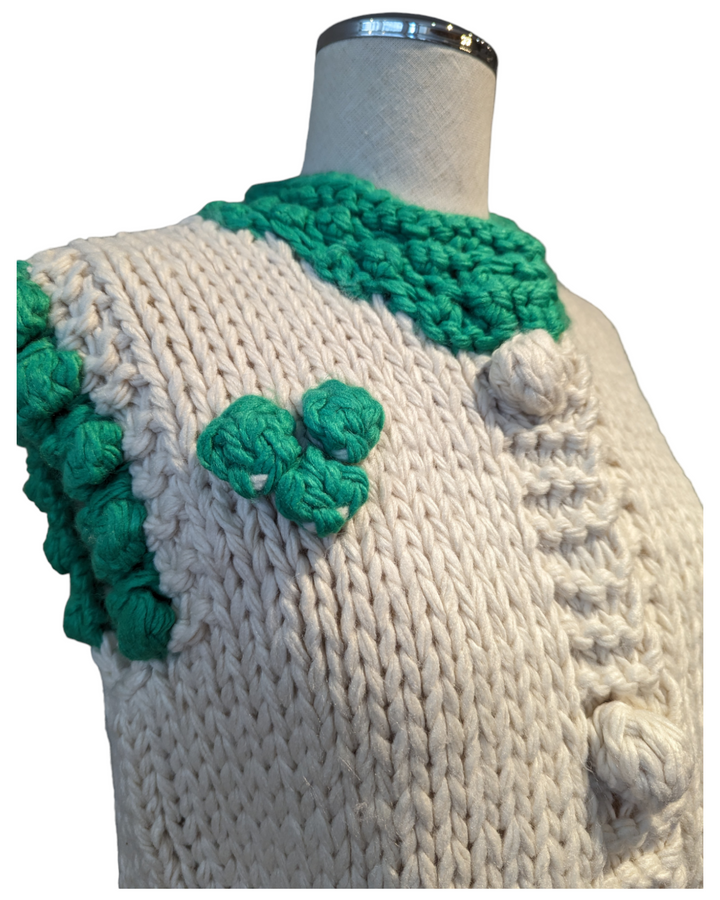 detail of the sweater vest showing the sleeve trim and the big knit flower accent 
