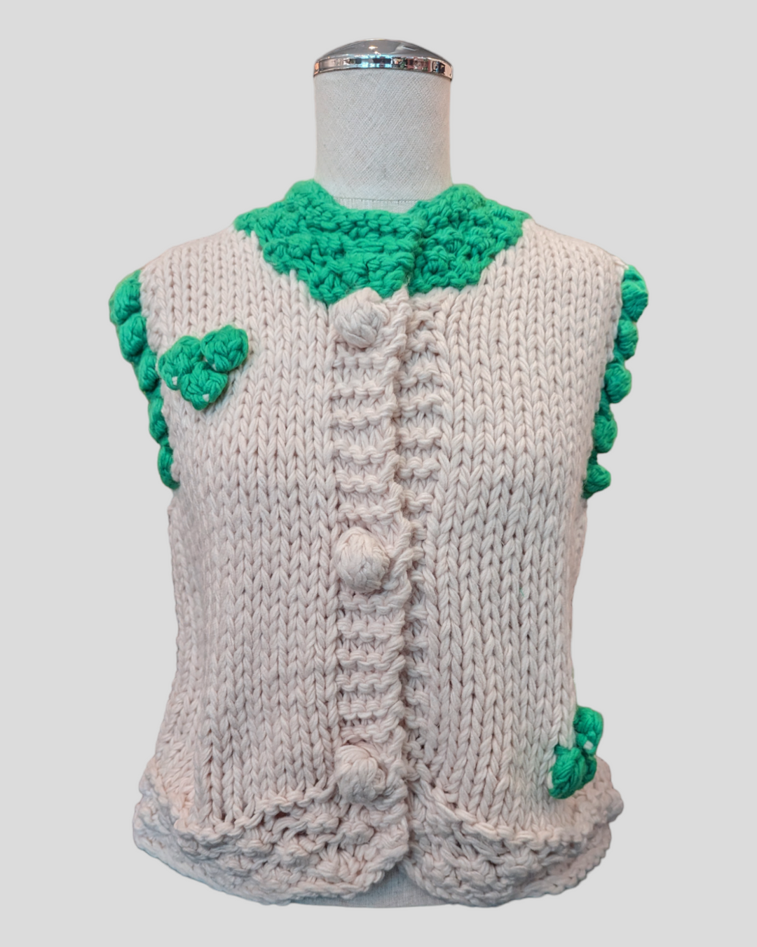 a fat open knit sweater vest in white and trimmed in green  on a mannequin
