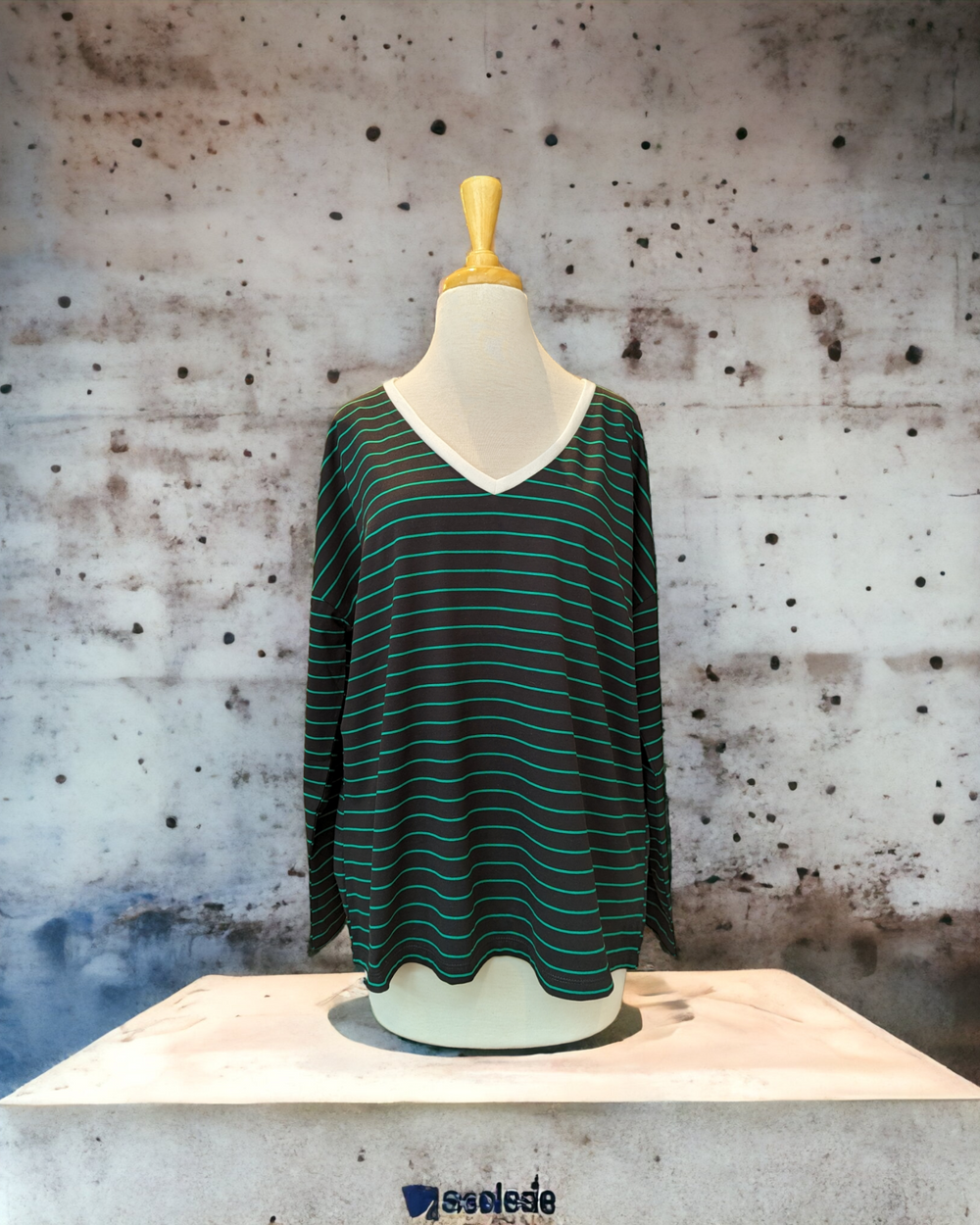a bleck and green stripe tee shirt on a white mannequin against a concrete wall