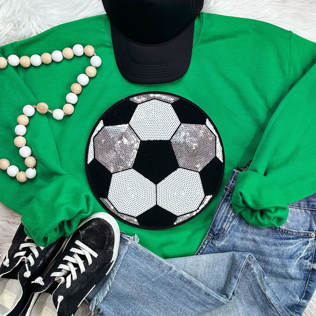 the sequin and soccer shirt are arranged in a flat lay with a beaded necklacem jeans a cap and black tennis shoes