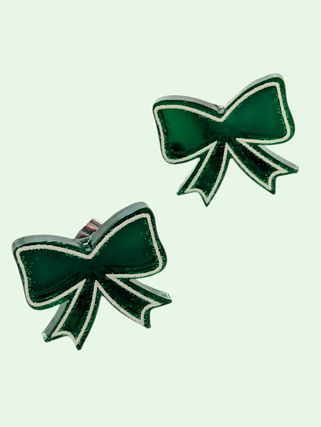 Green bow-shaped earrings on a light green background
