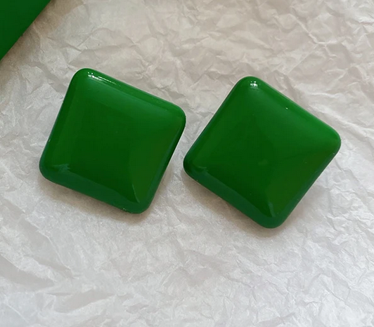 Two green square beads on a textured white surface