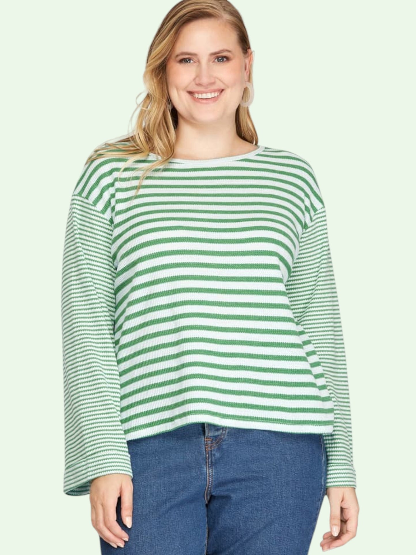 Woman wearing a green and white striped sweater and blue jeans on a light green background