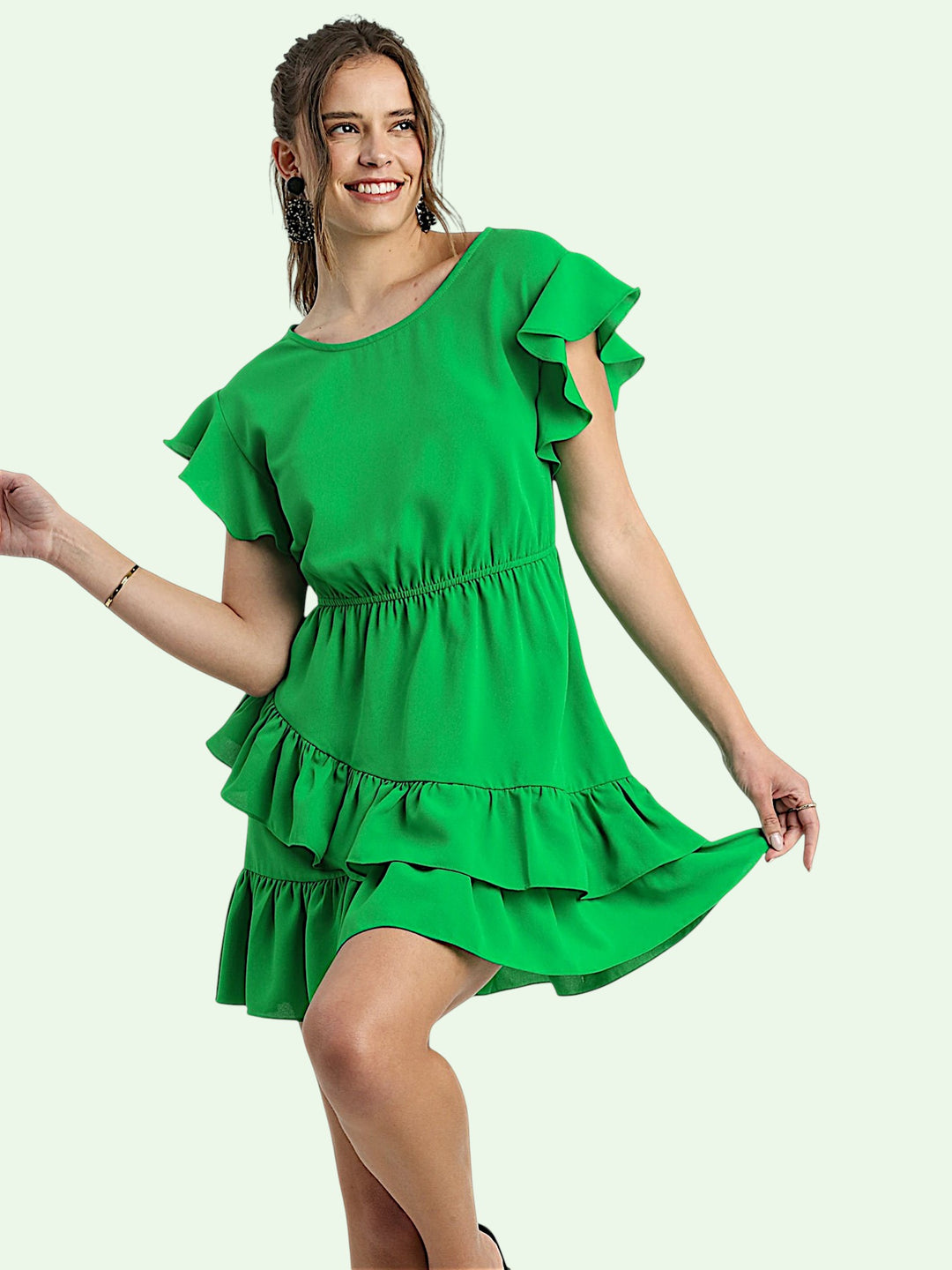Woman wearing a green dress with ruffled sleeves and bottom on a light green background