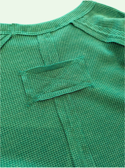 Close-up of a textured green knit garment, showing the fine woven fabric and a small rectangular patch detail on the back of the neck.