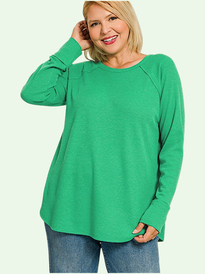 A woman wearing a bright green long-sleeve raglan top and blue jeans, posing against a light off-white background.