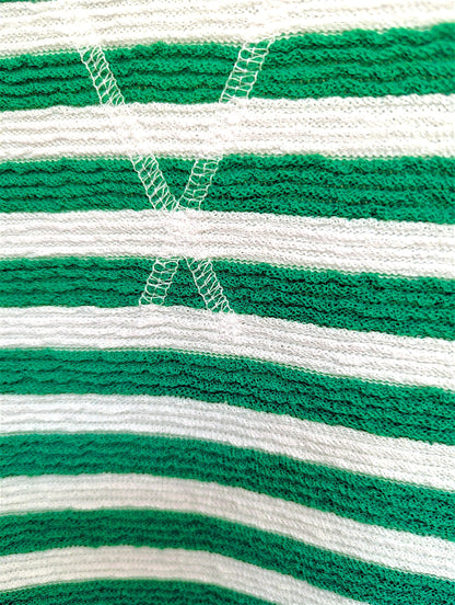 Close-up of a green and white striped knit fabric with a white embroidered cross motif.