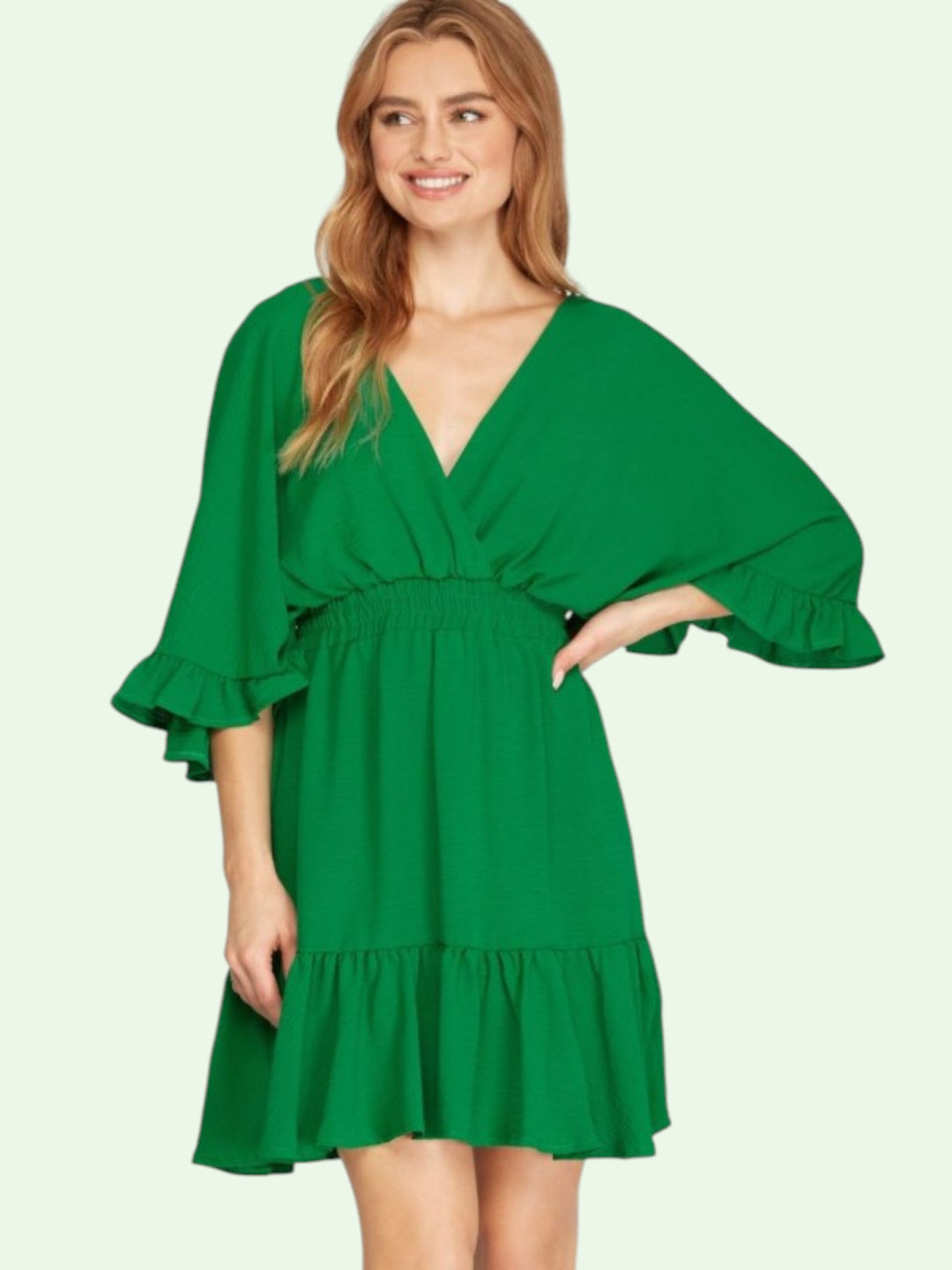 Woman wearing a green dress with ruffled sleeves on a light green background