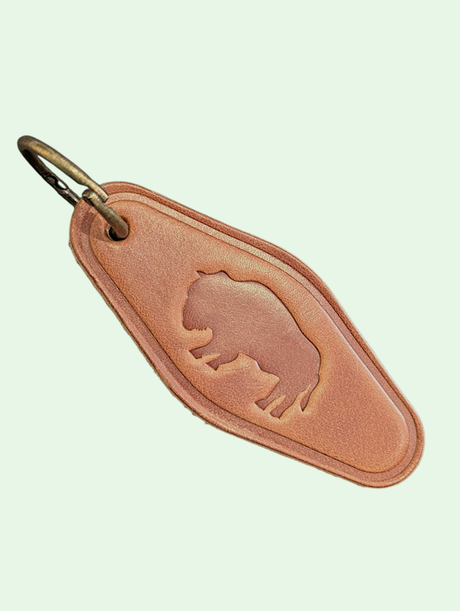 Brown leather keychain with bison silhouette on a light green background