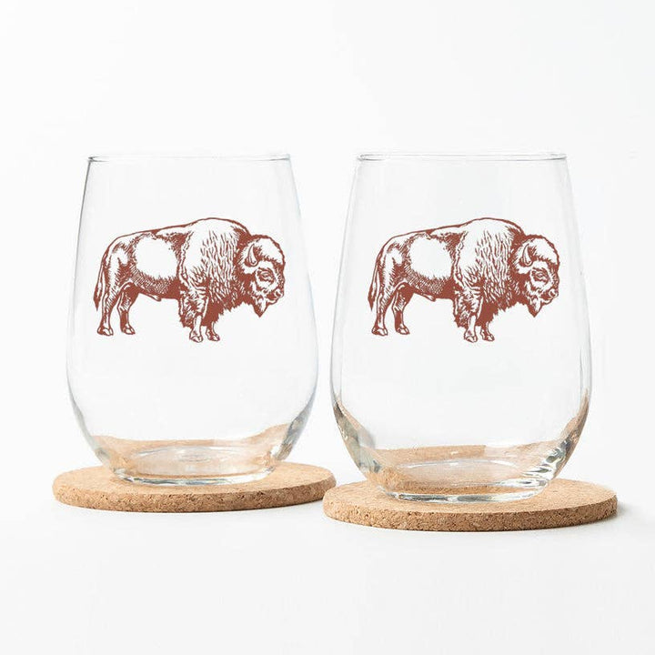 Two stemless wine glasses with bison illustrations on cork bases.