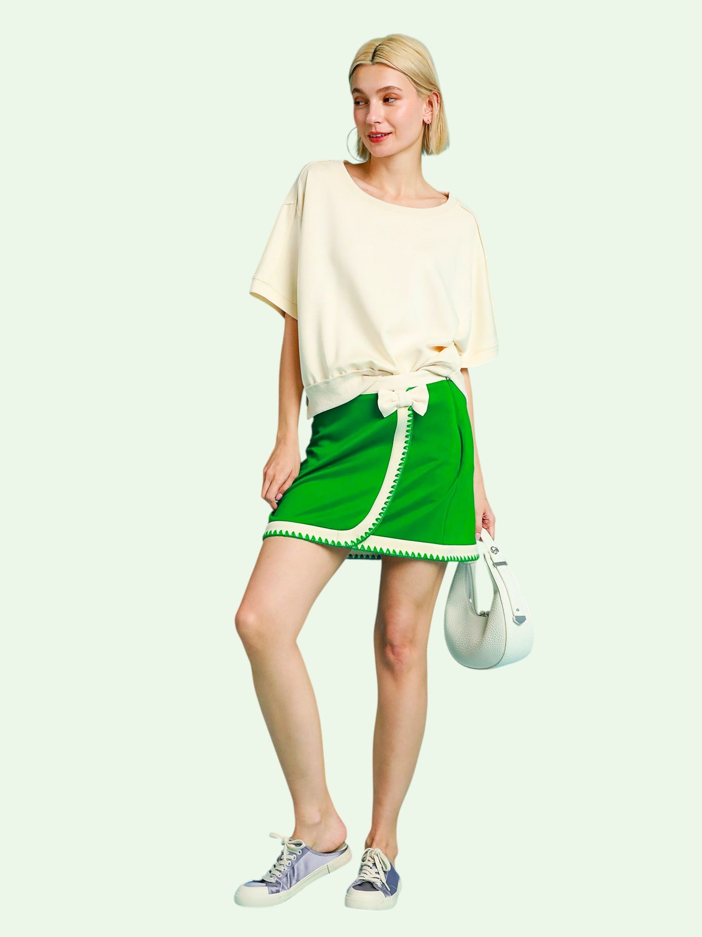 Woman wearing a green skort with white trim on a white background