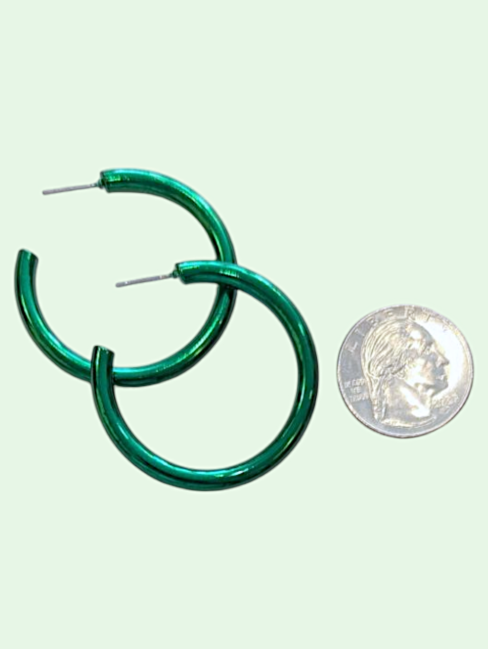 Green hoop earrings next to a silver coin on a light green background