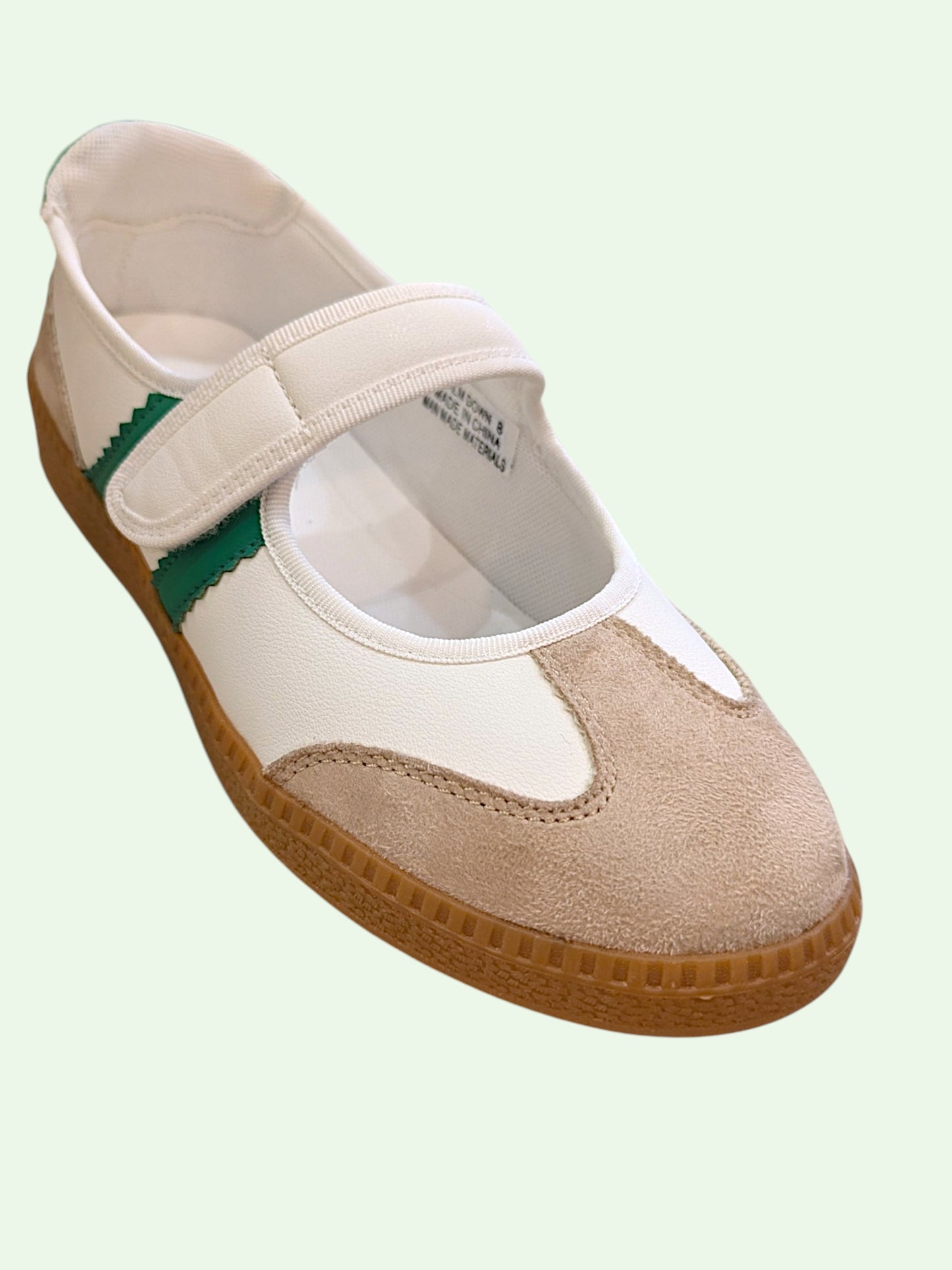 White and beige shoe with a green strap on a light green background