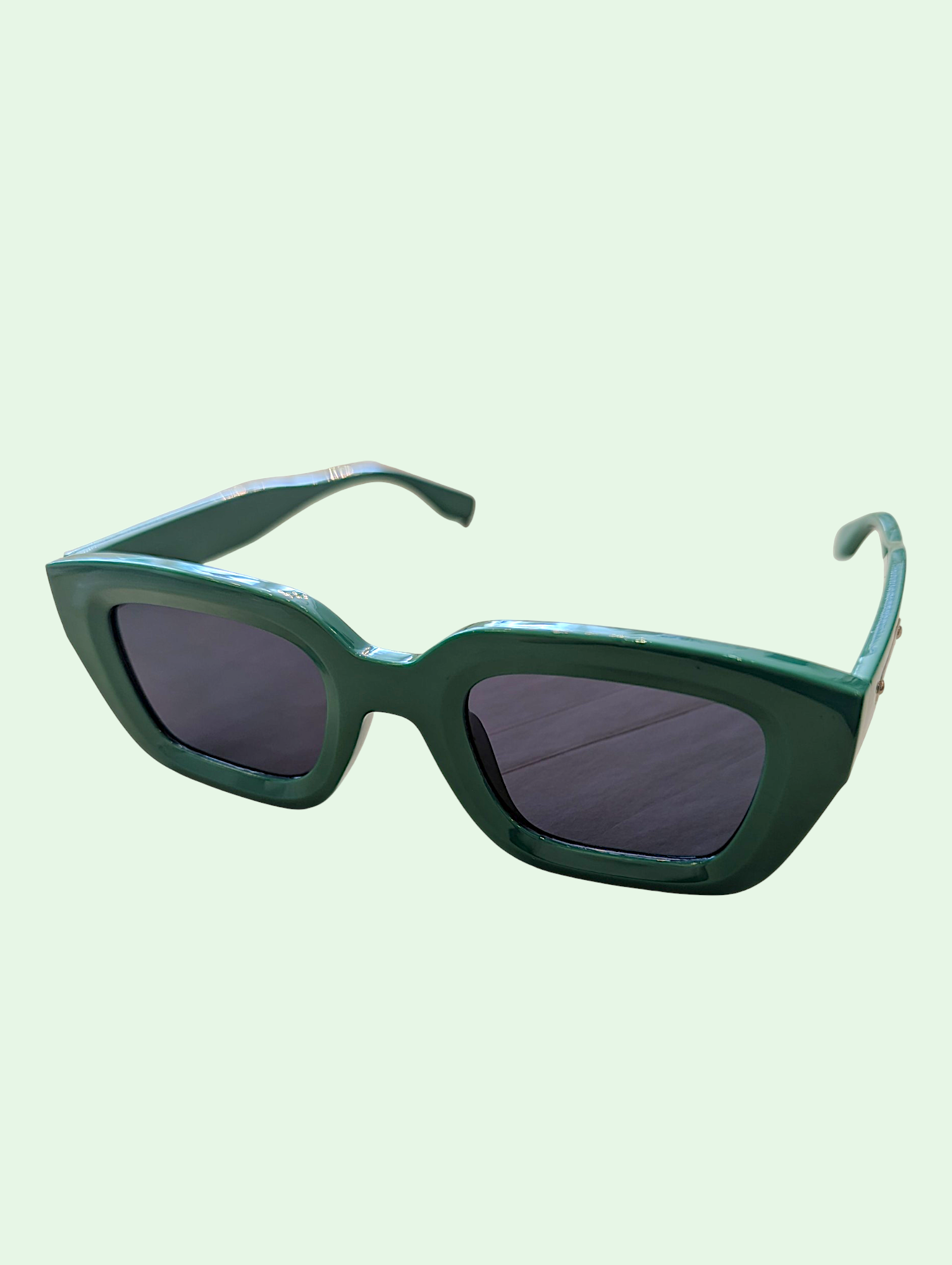 Green sunglasses with dark lenses on a light green background