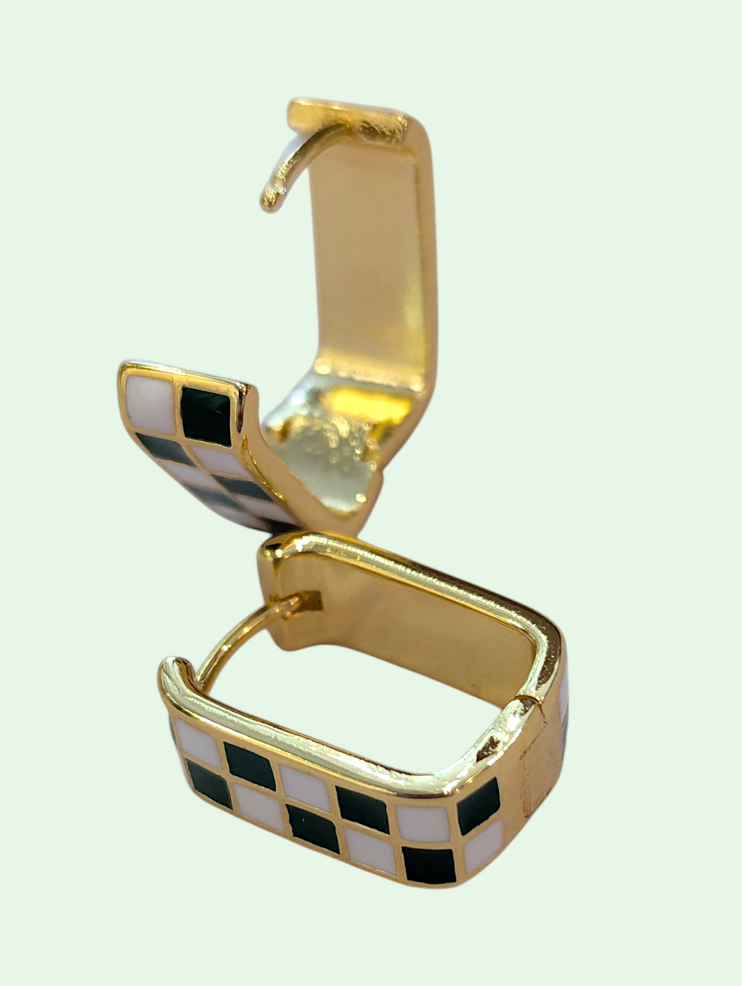 Gold and black checkered earring on a light green background