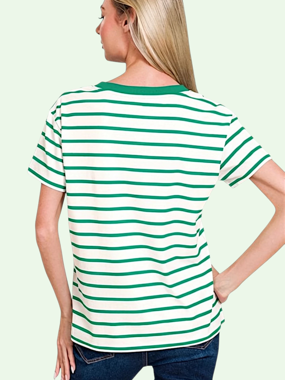 A woman shown from the back wearing a short-sleeve striped t-shirt with green and white horizontal stripes and a solid green crew neck, paired with dark blue jeans against a pale green background.
