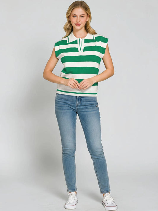 A woman modeling a green and white horizontally striped sleeveless knit top with a split collar, paired with light blue skinny jeans and white sneakers, against a light gray studio background.