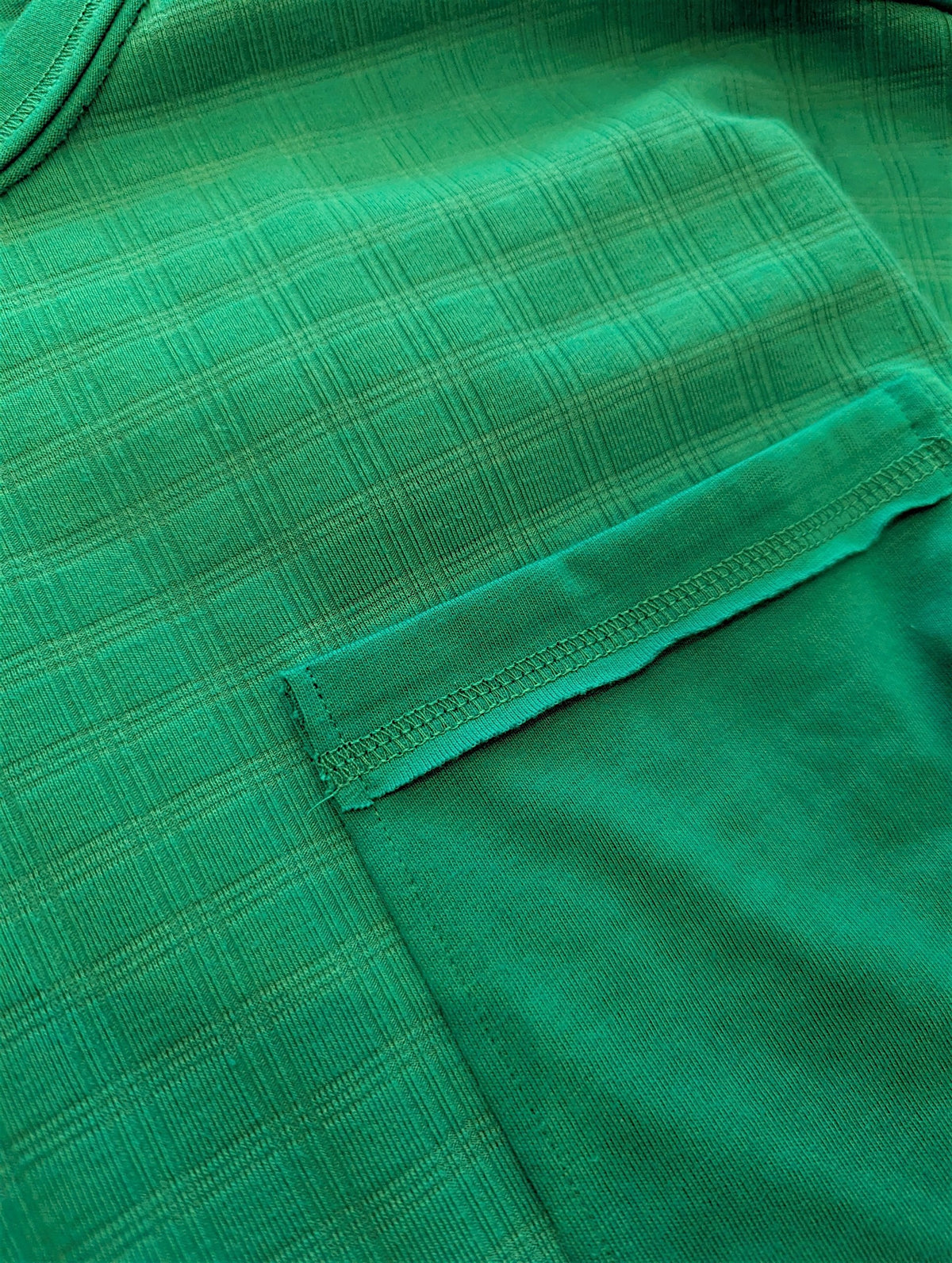 Close-up of a green fabric garment with a pocket and visible stitching.