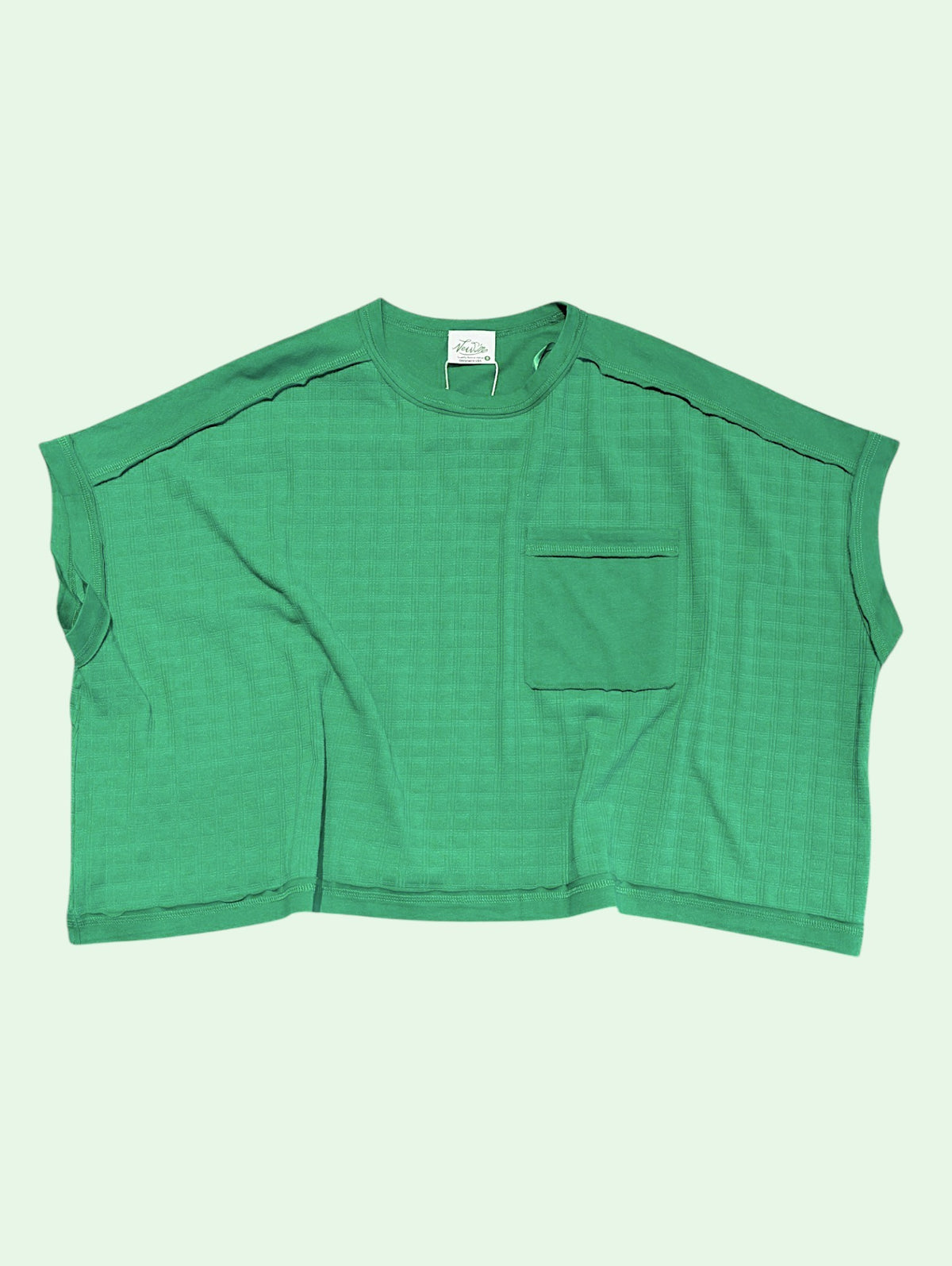 A green cropped knit top with a chest pocket and contrast stitching, laid flat against a pale mint green background.