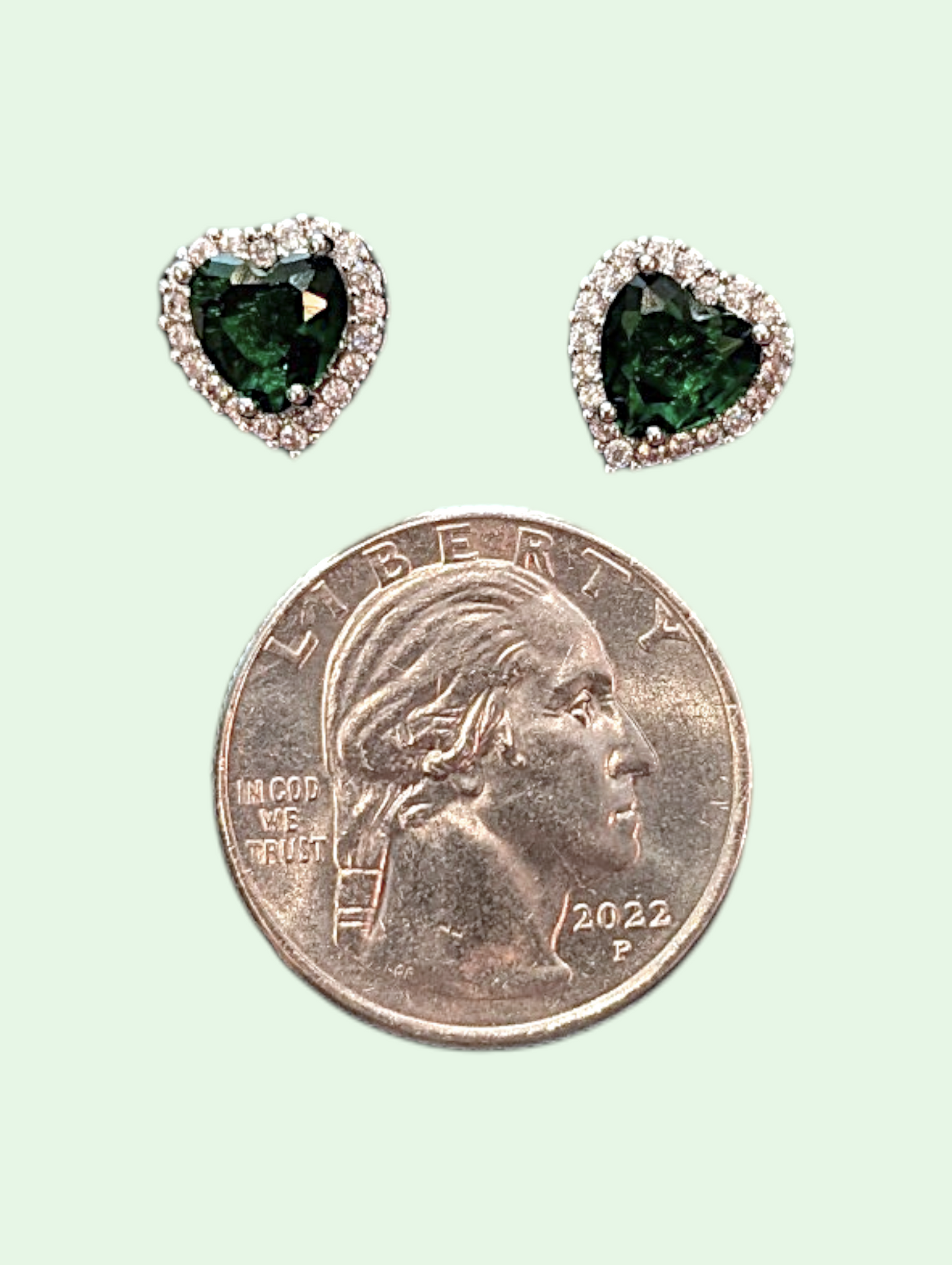 Heart-shaped green gemstone earrings next to a quarter on a light green background
