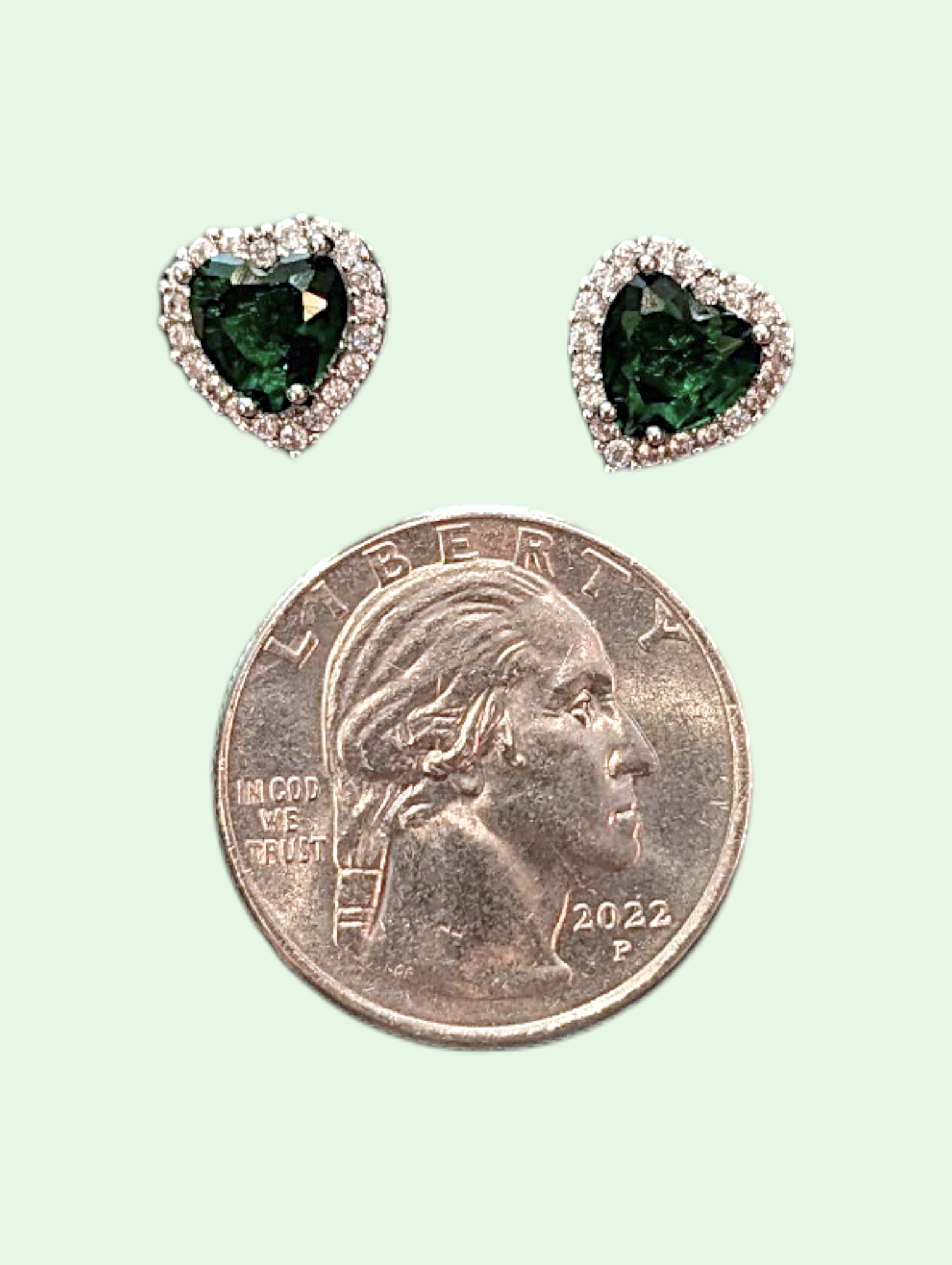 Heart-shaped green gemstone earrings next to a quarter on a light green background