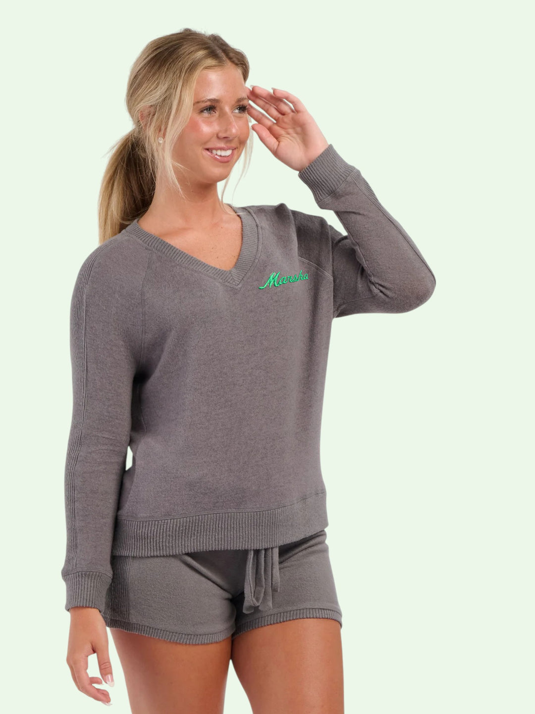Woman wearing a gray sweater and shorts set with a logo on a light green background