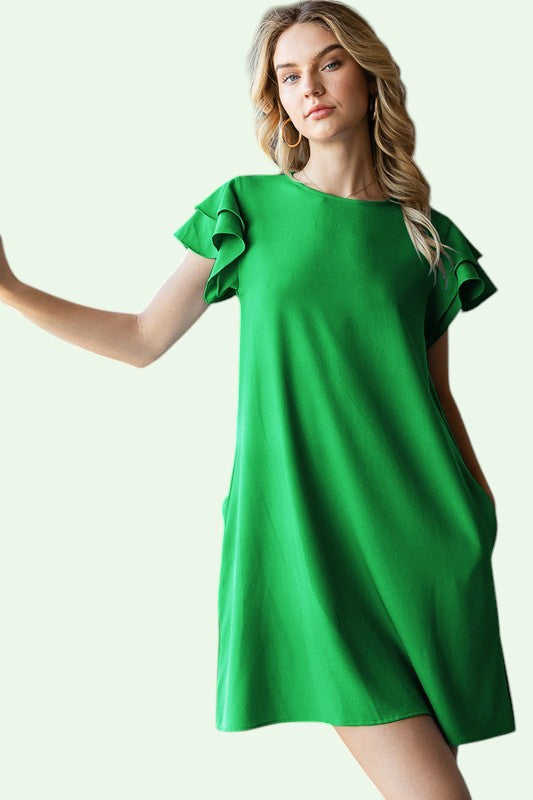 Woman wearing a green dress with ruffled sleeves on a light green background