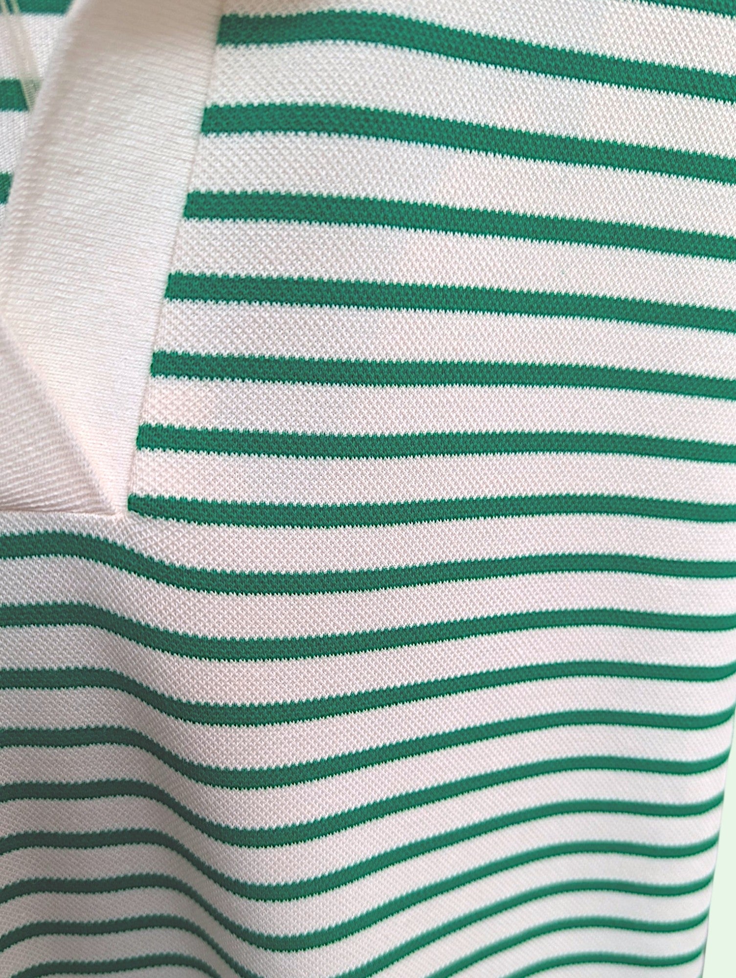Close-up of a white knit fabric with thin horizontal green stripes and a folded collar.