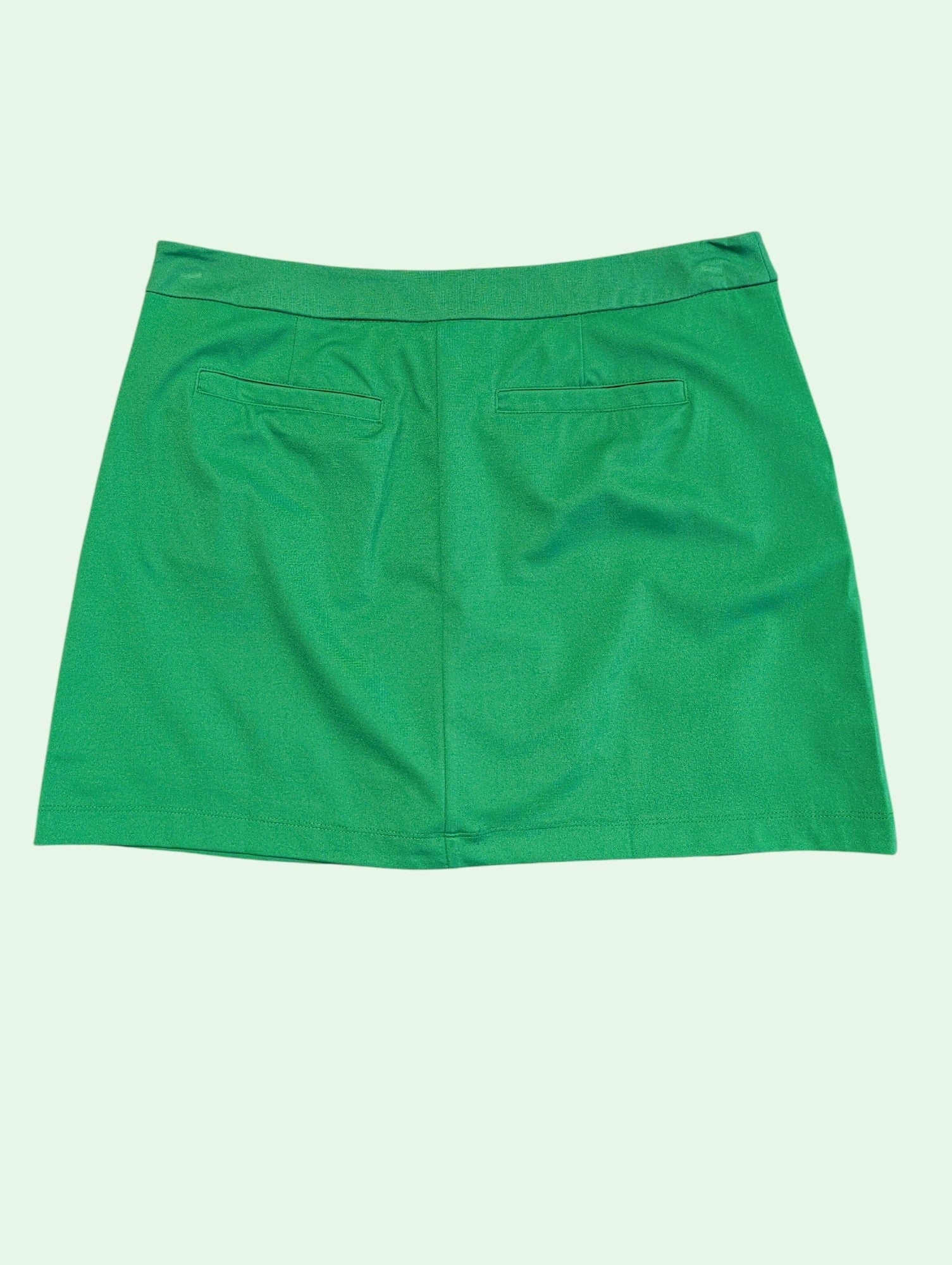 A bright green mini skirt with two front patch pockets, shown flat against a pale mint green background.