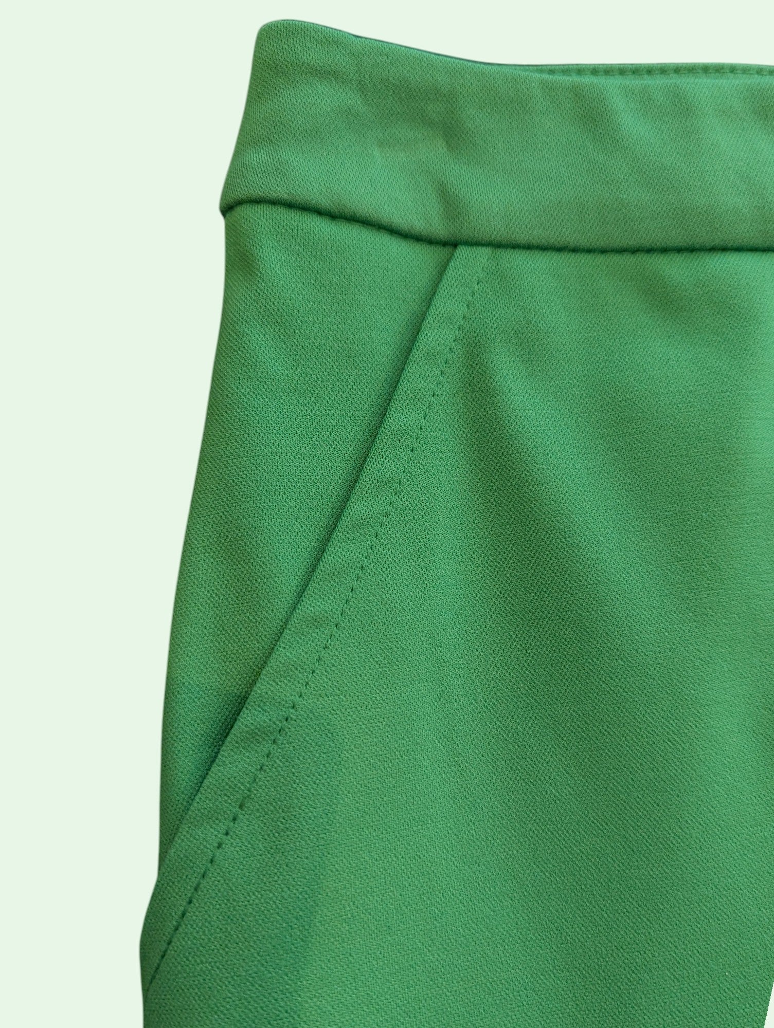 Close-up of a bright green fabric garment, showing the waistband and side seam details against a pale mint background.