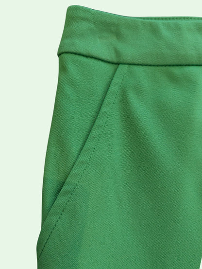 Close-up of a bright green fabric garment, showing the waistband and side seam details against a pale mint background.