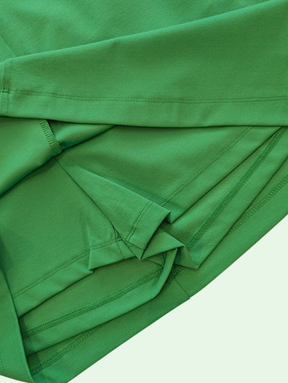 A close-up of folded green athletic fabric, showing the texture and stitching details against a very light off-white background.
