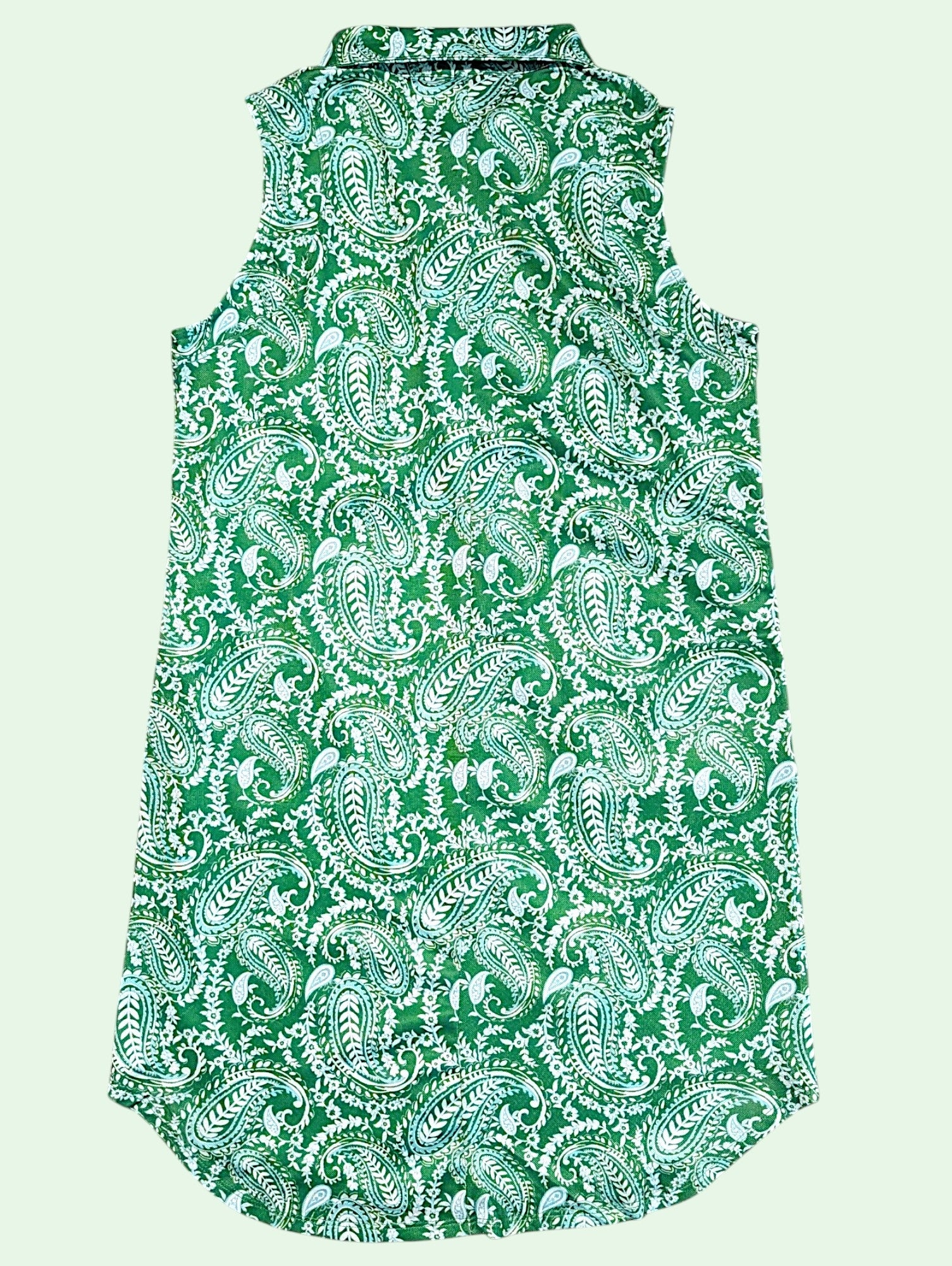 A sleeveless collared shirt dress featuring an all-over green and white paisley pattern, shown against a solid pale green background.