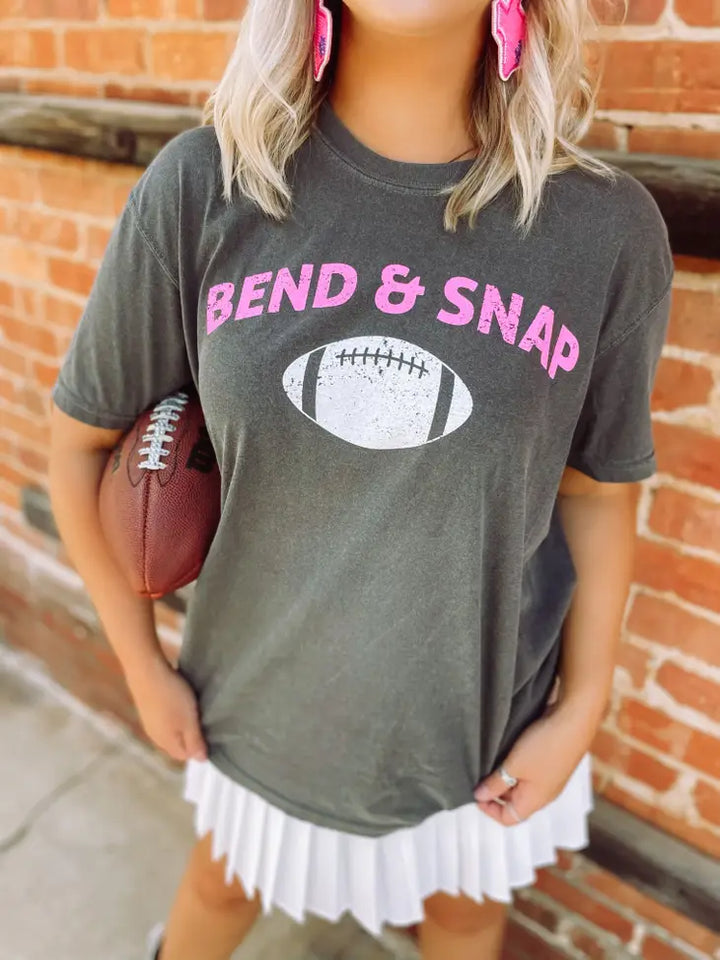 Model standing in front of brick wall holding football wearing gray shirt with Pink writing and white football graphic