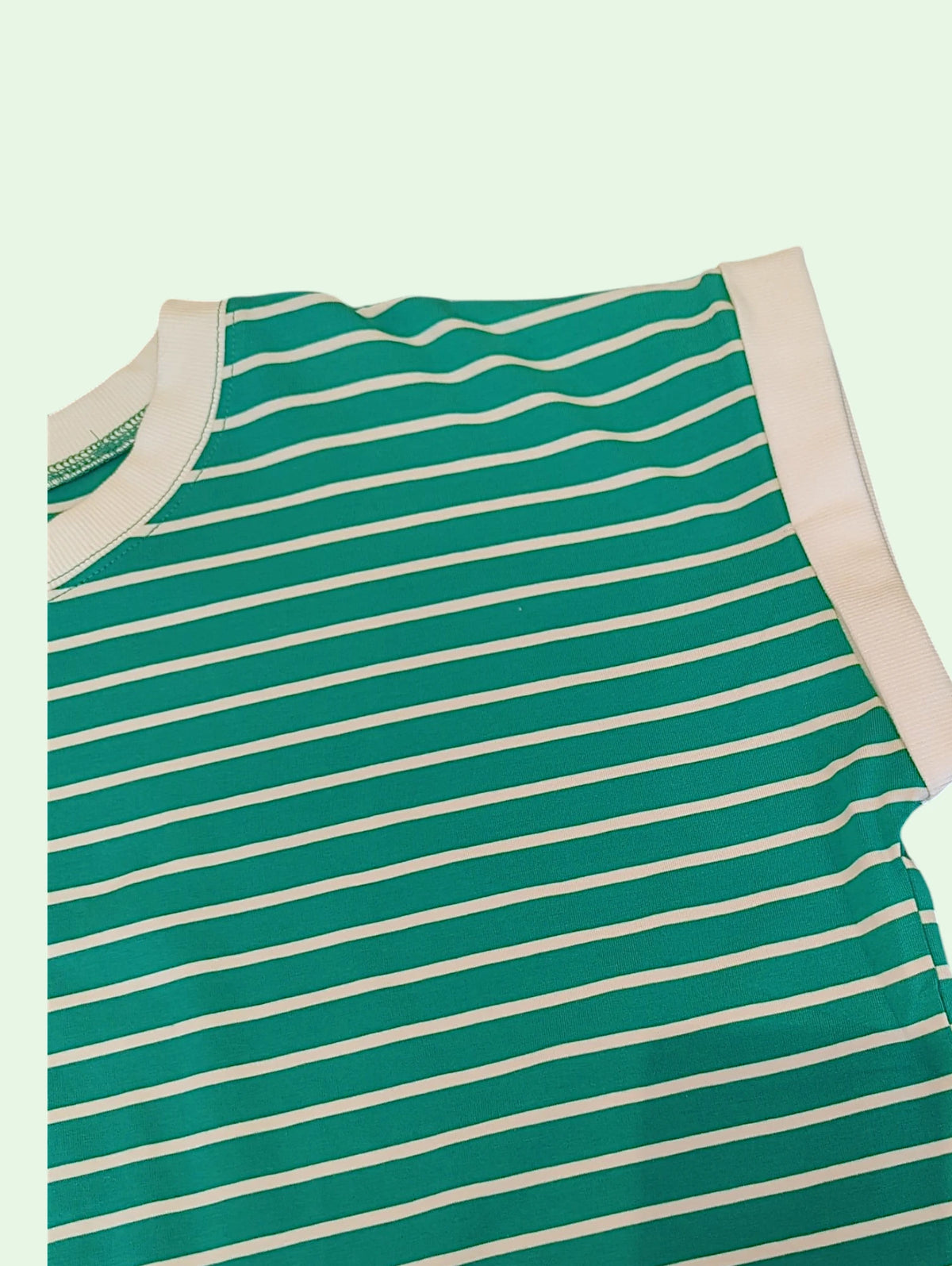 A close-up of a green and white striped sleeveless top or dress, showing the striped pattern and solid light pink trim on a pale mint green background.
