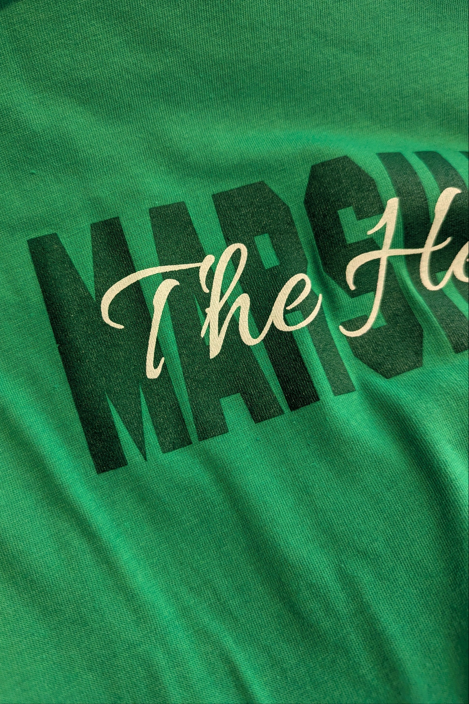 Close-up of a green t-shirt featuring a graphic print with the word 'MARCH' in bold black letters and 'The He.
