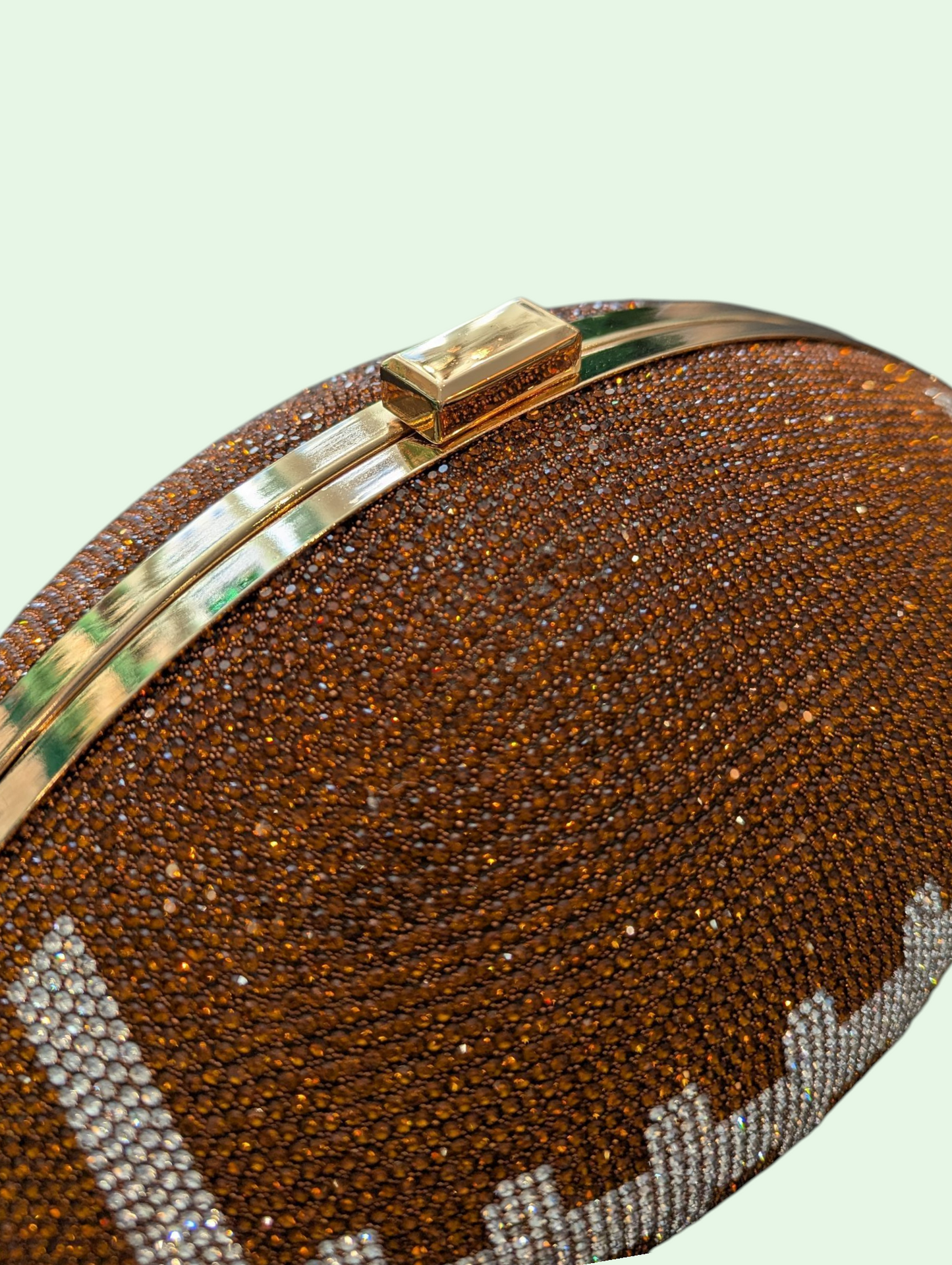 Brown glittery clutch with gold accents on a light green background
