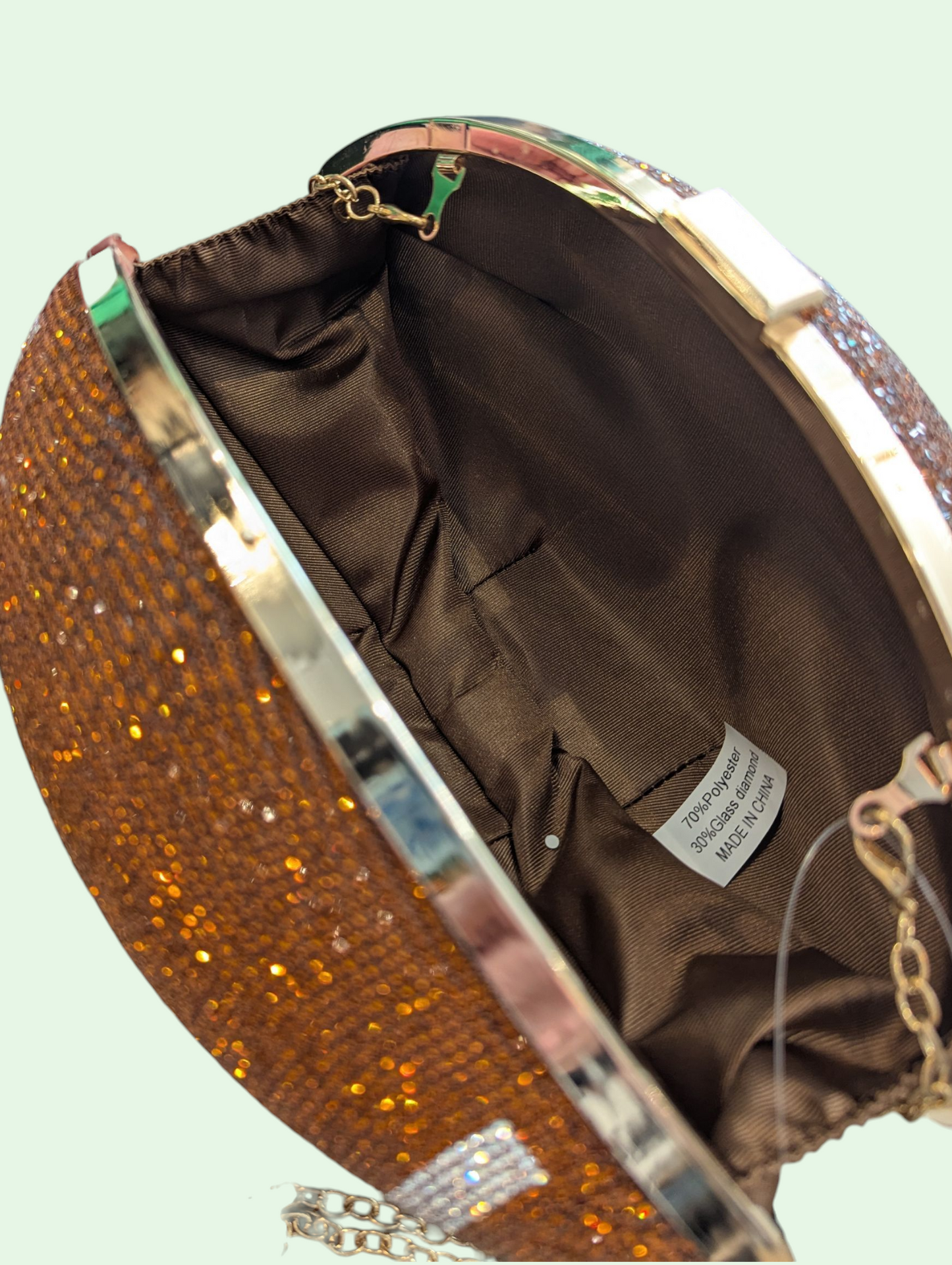 Close-up of a glittery handbag with a visible brand label on a light green background