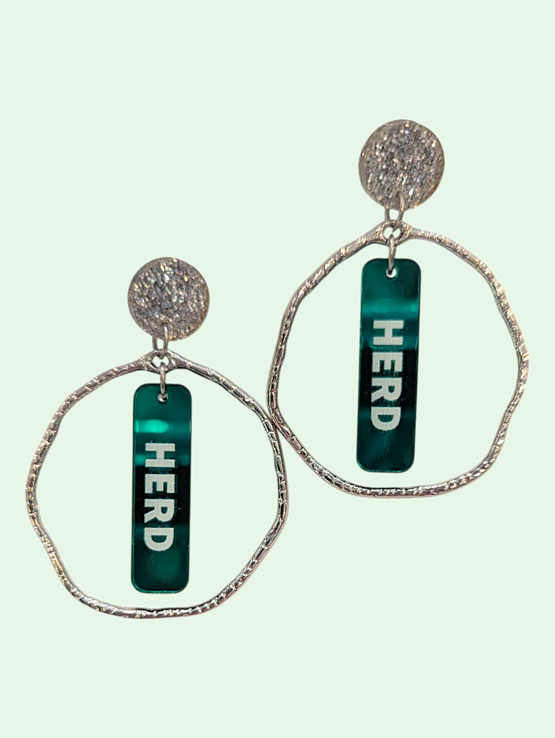 Earrings with 'HERD' text on green bars against a light green background