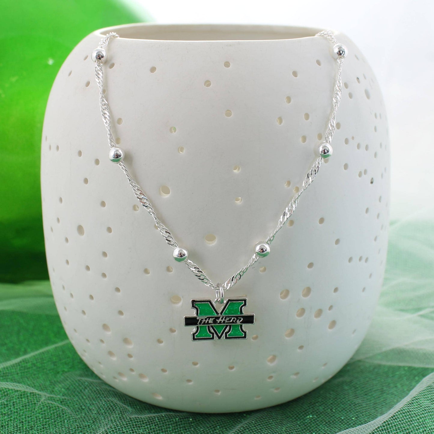 Necklace with a pendant featuring a 'M' logo on a white textured vase against a green background