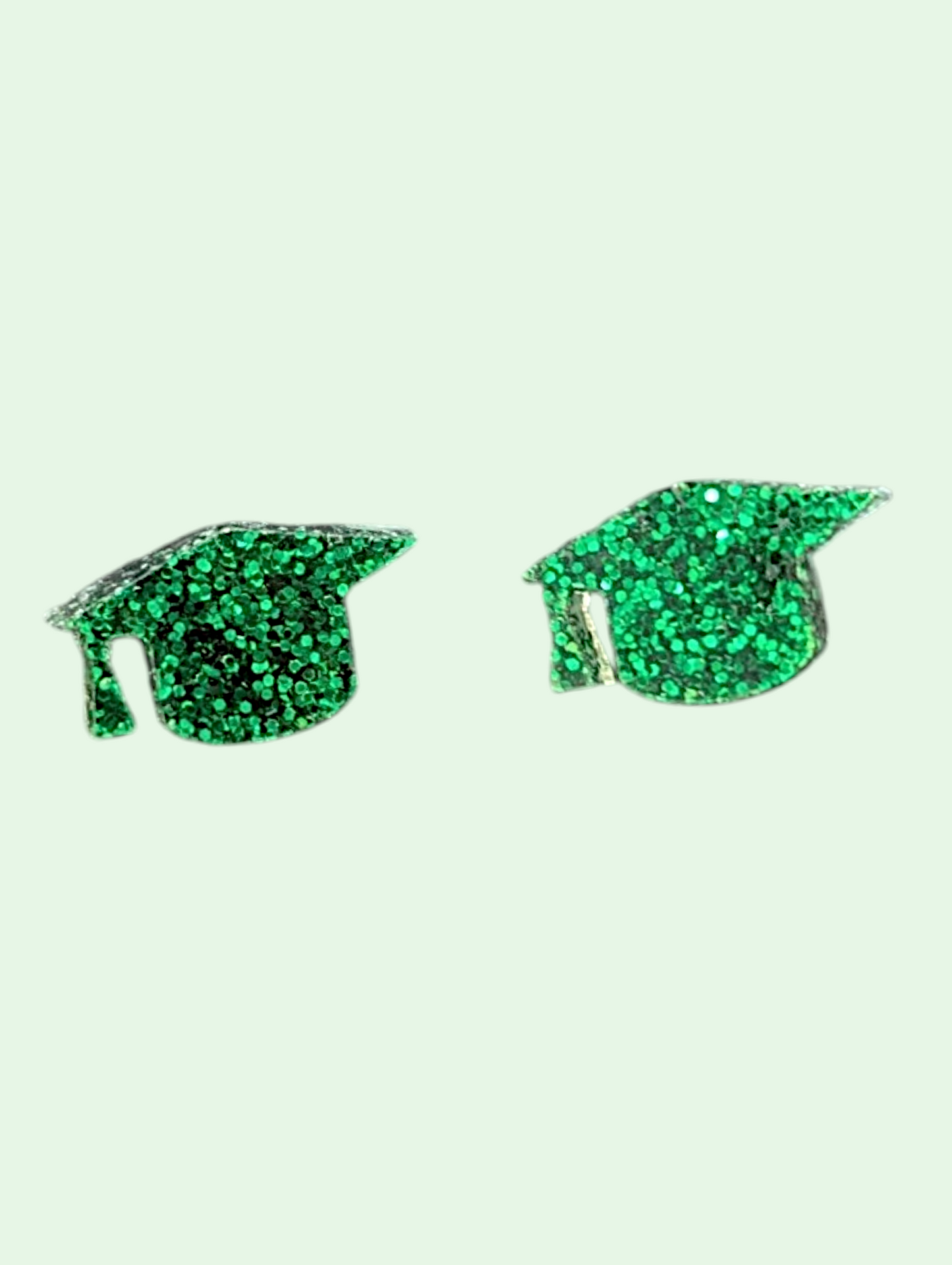Green glittery graduation cap earrings on a light green background