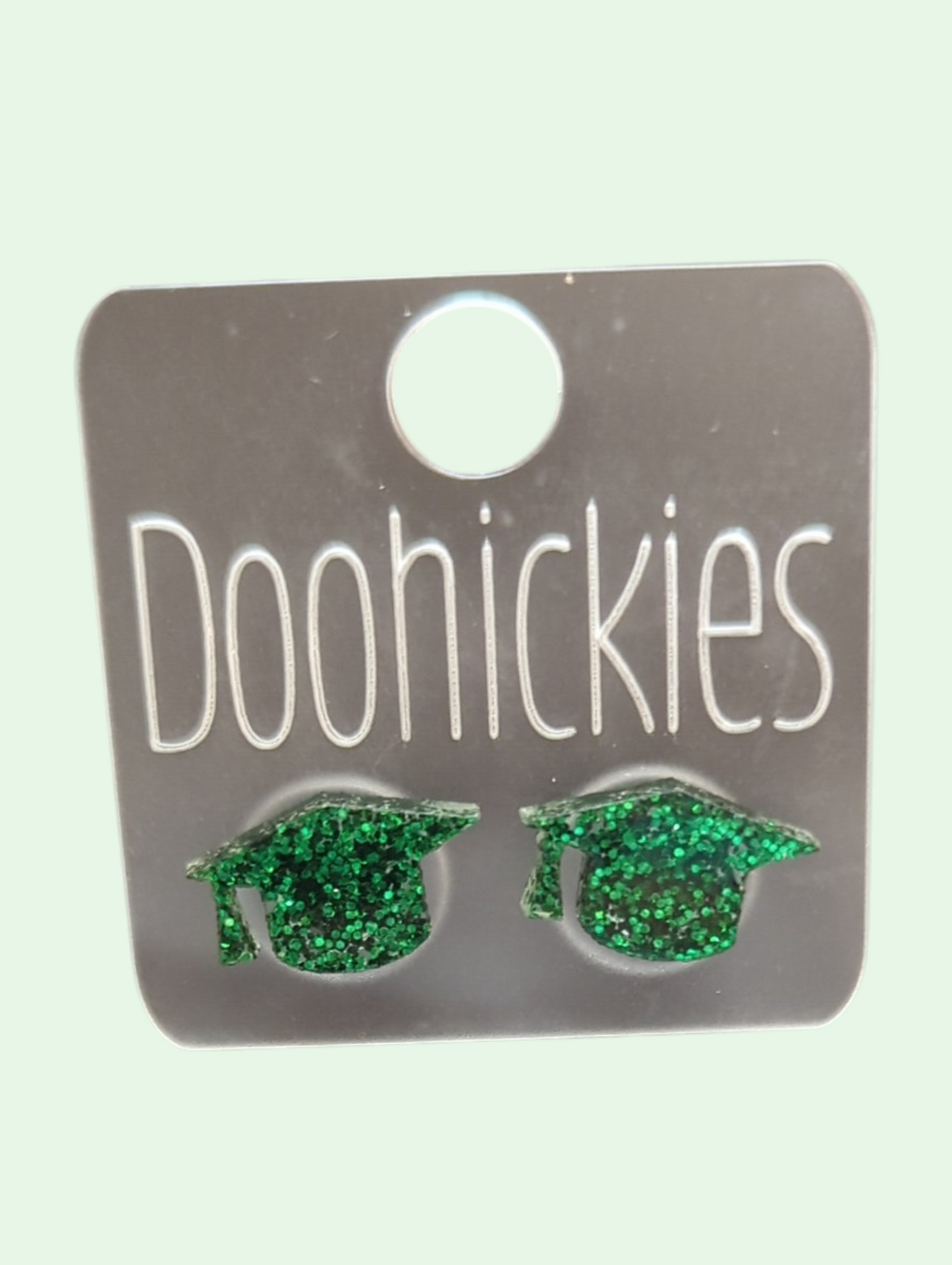Green glittery graduation cap earrings on a Doohickies card.